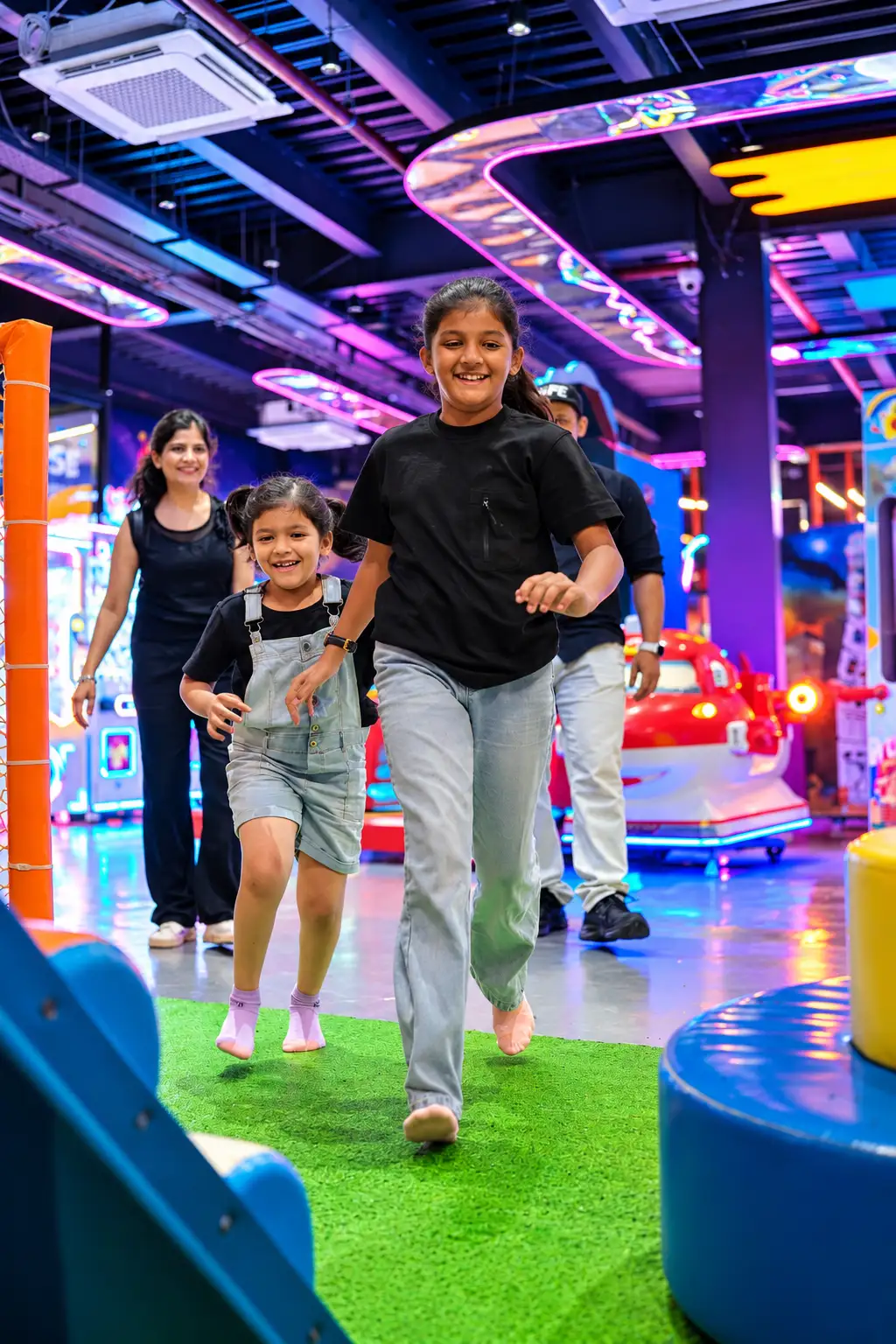 Children and a parent running across the Funiverse play floor, smiling